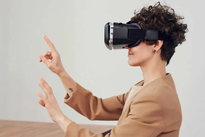 Mulher usando óculos de realidade virtual (RV), interagindo com o ambiente virtual por meio de gestos com as mãos.