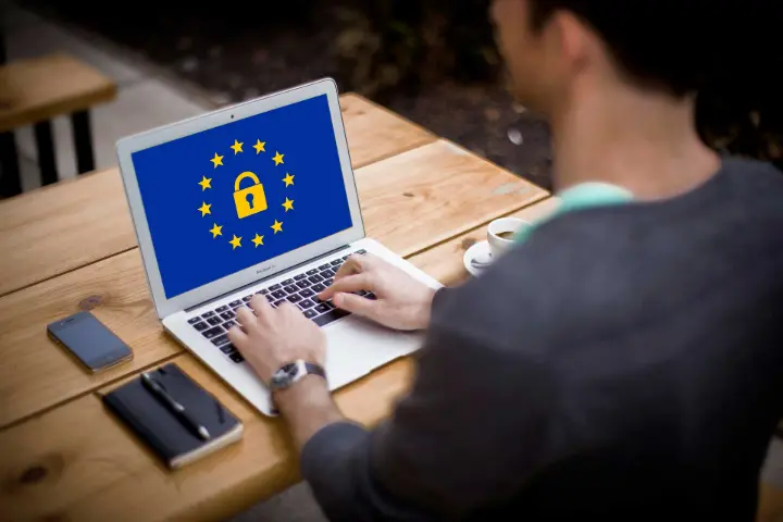 Pessoa usando um laptop exibindo a bandeira da UE com um cadeado, significando privacidade online.