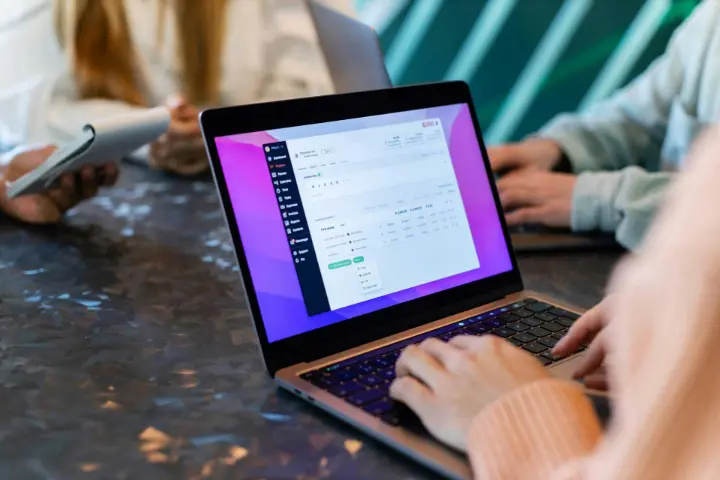 Close de mãos digitando em um laptop exibindo um aplicativo de gerenciamento de dados.