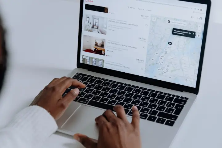 Pessoa usando um laptop para navegar em listagens on-line de apartamentos ou quartos para alugar, mostrando diversas imagens de interiores e um mapa.