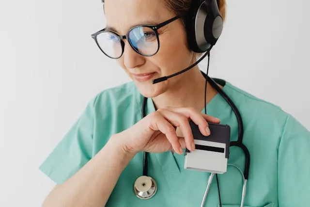 Profissional médica com uniforme azul-petróleo, óculos, fone de ouvido e segurando um carimbo.